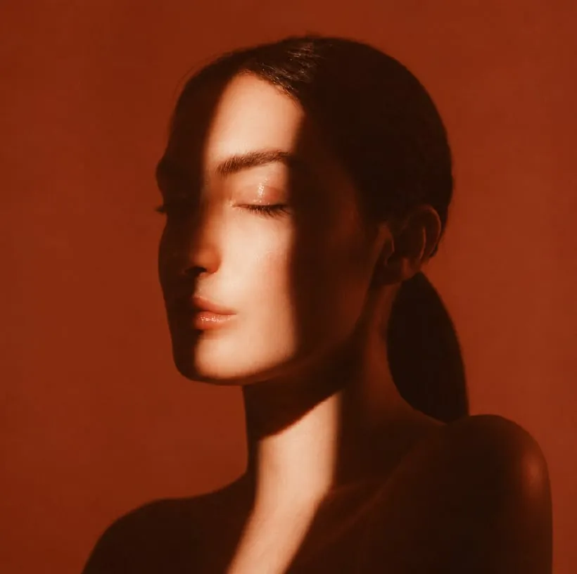 Retrato en luz cálida sobre fondo terracota — piel real, sin retoques